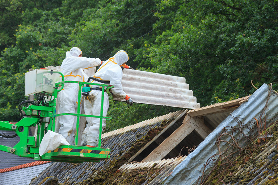 Two operators wearing PPE removing asbestos roofing