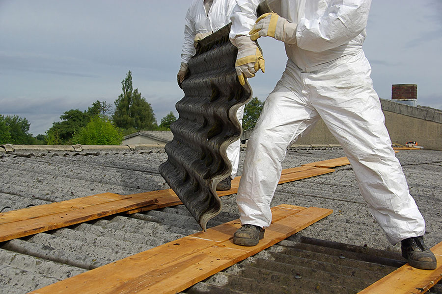 Two workers in full PPE removing asbestos roof tiles