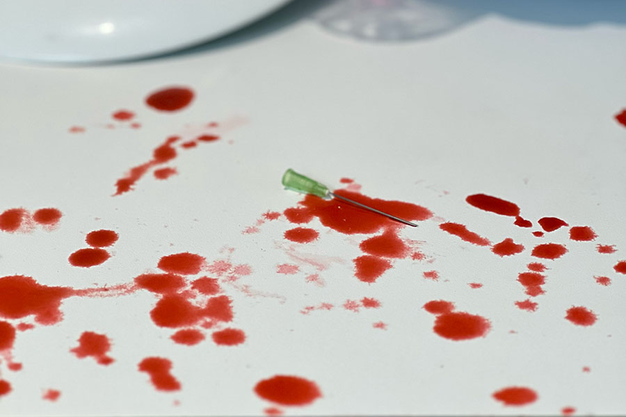 A blood spattered work surface with a hypodermic needle in the middle