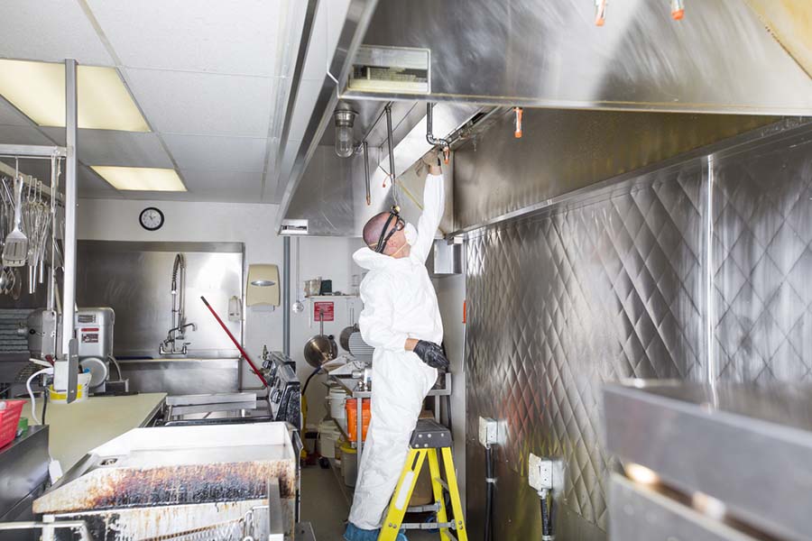 A worker performing a full deep clean of an industrial kitchen