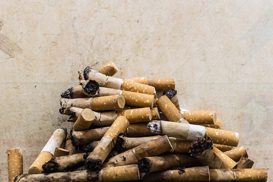 A pile of cigarette butts in front of a nicotine stained wall