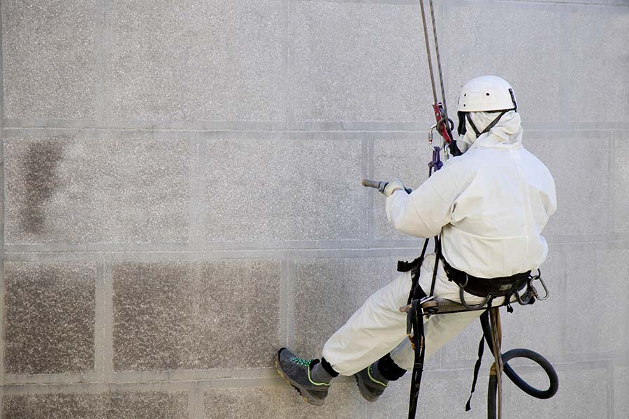 A worker wearing a protective gear cleaning a stone exterior with sandblasting equipment