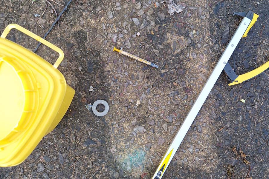 A sharps disposal box, sharps picker and syringe laying on the floor during a needle sweep