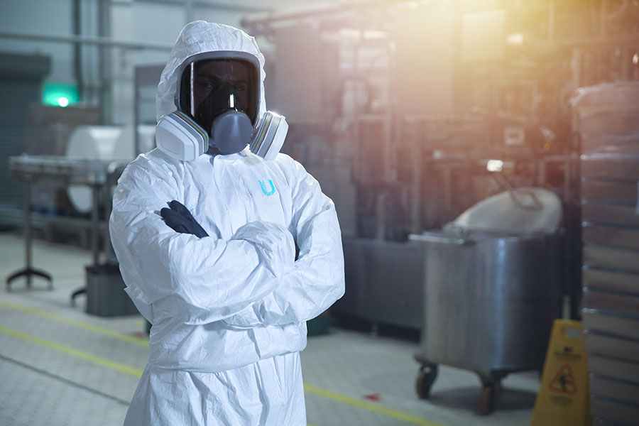 A person wearing an Ultima branded full PPE suit stands with their arms folded